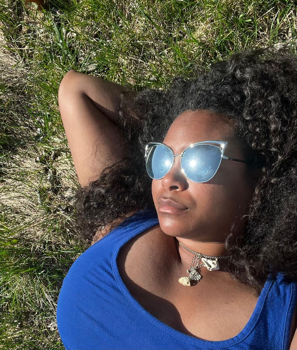 Woman lying in the grass with blue top and custom necklace with drop pendant of three seashells.